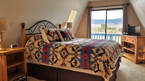 Une chambre à coucher comprenant un lit, une table de chevet, un bureau, une télévision et une fenêtre donnant sur l’extérieur.