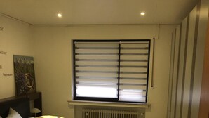 Un dormitorio con cama, radiador, ventana con persianas y armario.