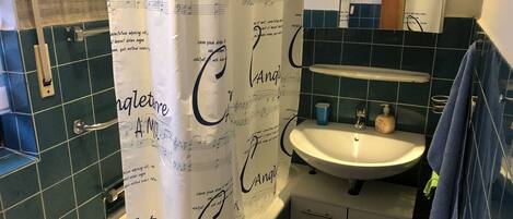 A bathroom with a white sink, a mirror, and a shower curtain with musical notes and text.