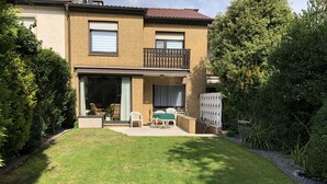 Una casa de dos pisos con un balcón, un patio con mesa y sillas, y un césped cuidado.