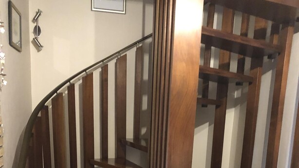 Una escalera en espiral de madera con barandilla de metal, que lleva a un piso superior.
