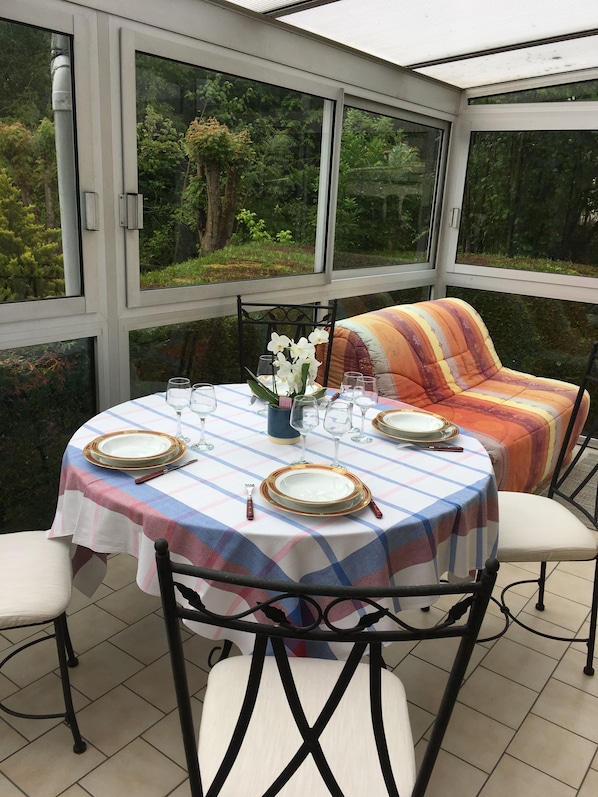 A conservatory with a table set for dining, surrounded by chairs and a cushioned bench.