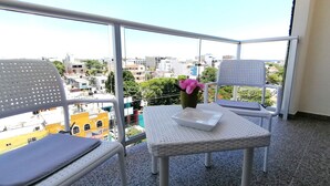 Ein Balkon mit zwei weißen Stühlen, einem kleinen Tisch und einer Blumenvase.