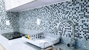 Eine Küche mit Granit-Arbeitsplatte, Spüle aus Edelstahl, Geschirrgestell und einer Rückwand mit Mosaikfliesen.