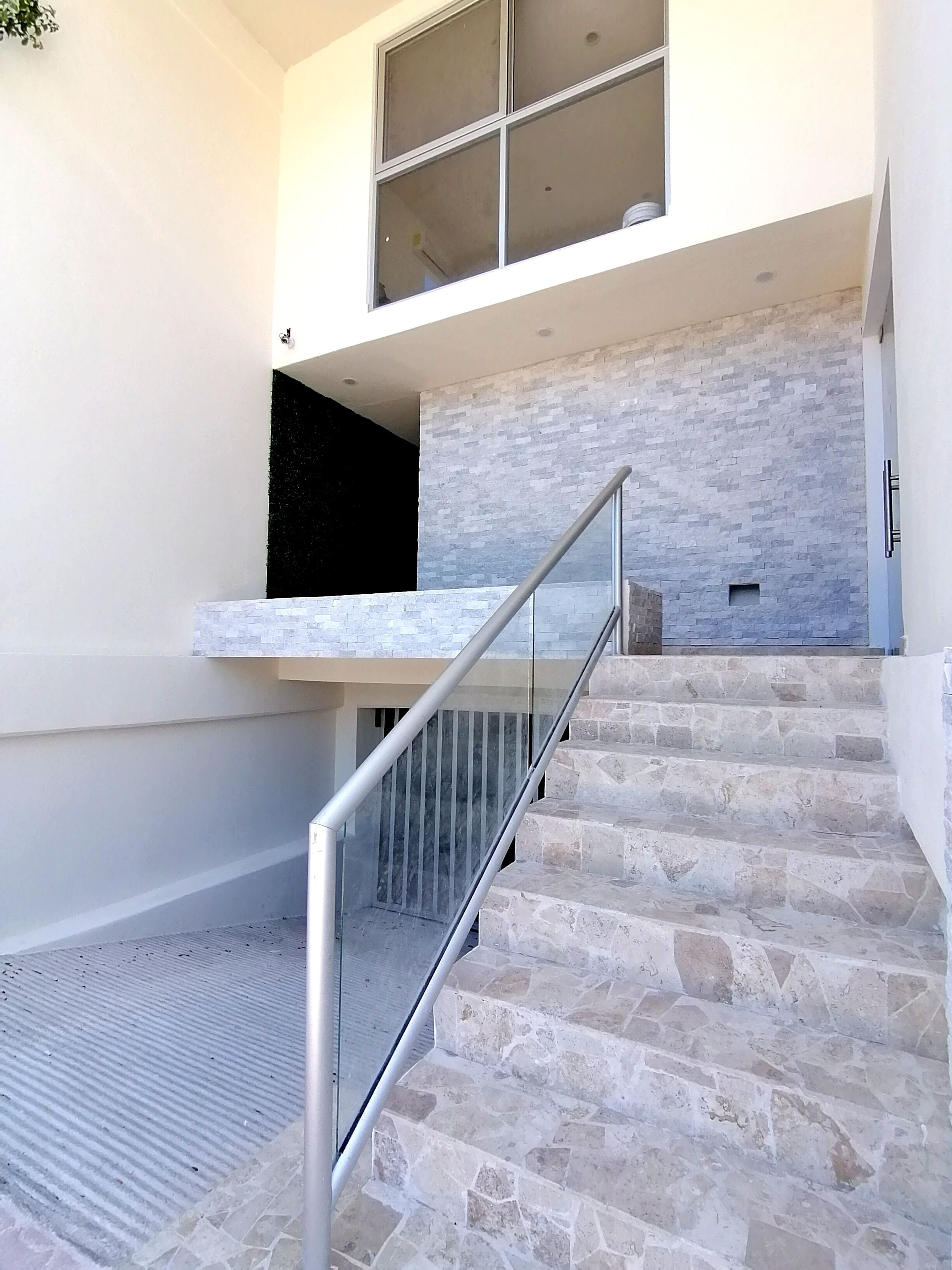 Eine Treppe mit Steinstufen und einem Metallgeländer, die zu einem Zwischenpodest mit einer Glastür führt.