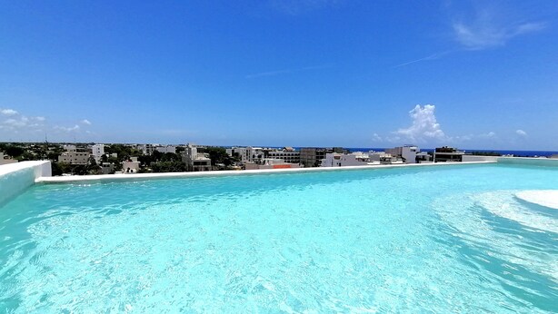 Ein klares, blaues Schwimmbecken mit Blick auf einen Strand und Gebäude im Hintergrund.