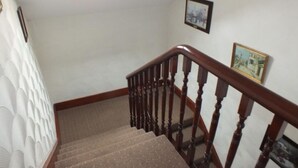 Un escalier avec des rampes en bois et des marches recouvertes de moquette, menant à un palier.