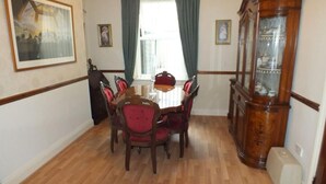 Un coin repas comprenant une table et des chaises en bois, un meuble avec des portes en verre et une fenêtre avec des rideaux.