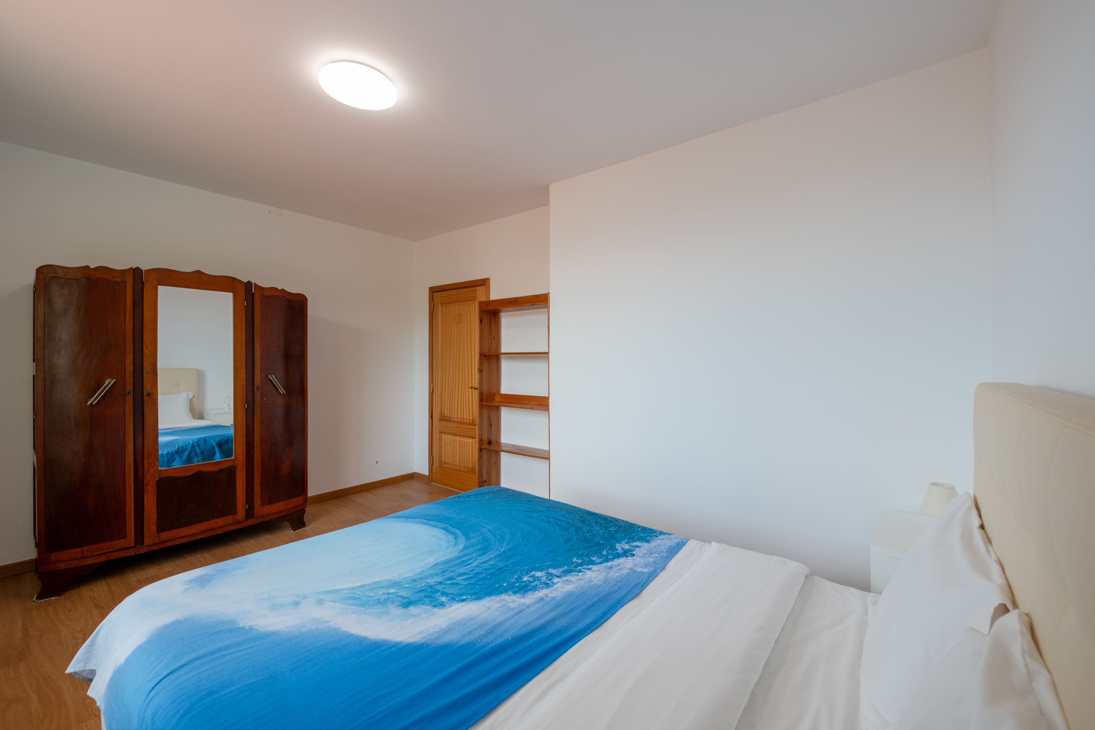 A bedroom with a bed, wooden wardrobe, and a nightstand.