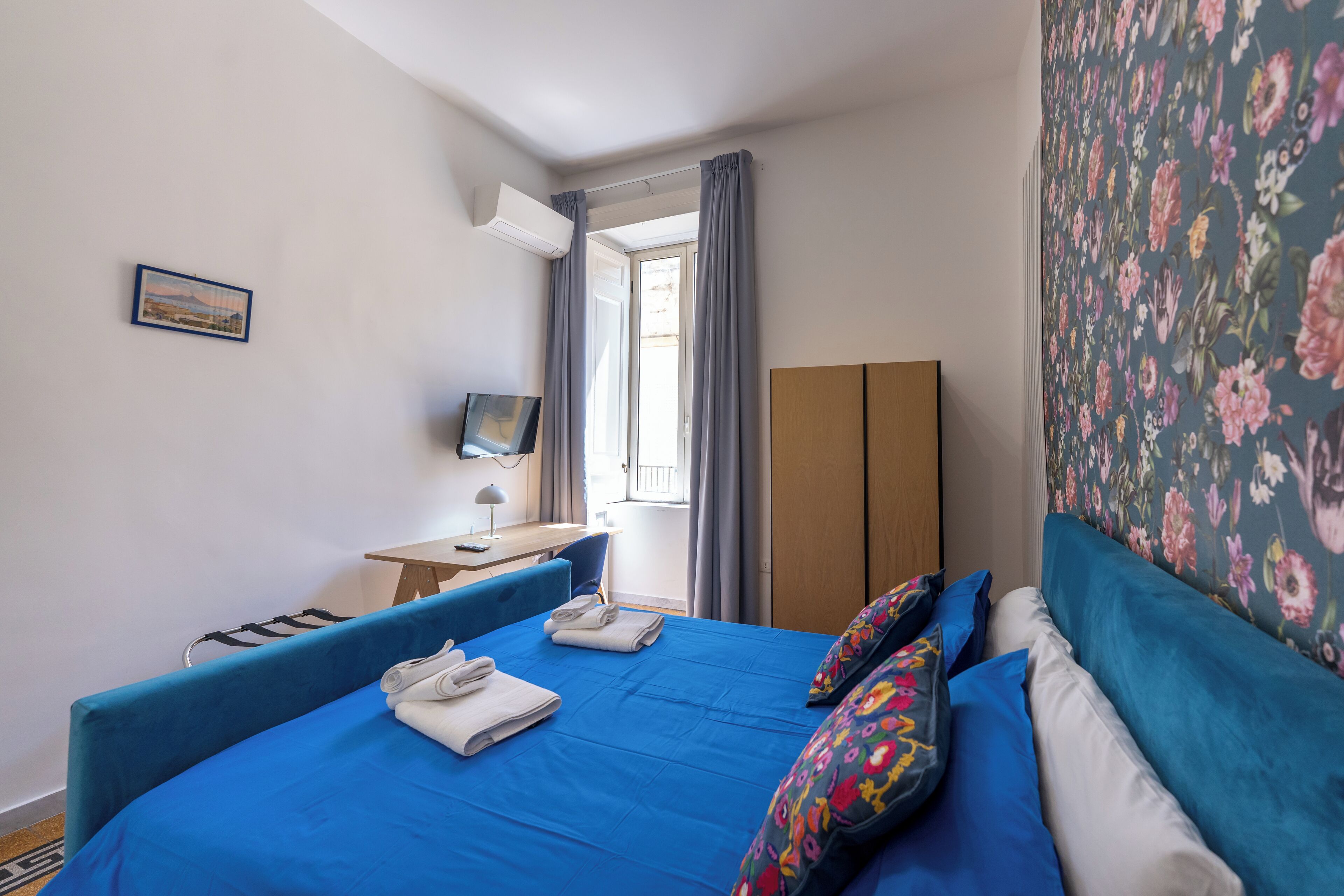 A hotel room with a bed, a desk, a chair, a TV, and a wardrobe.