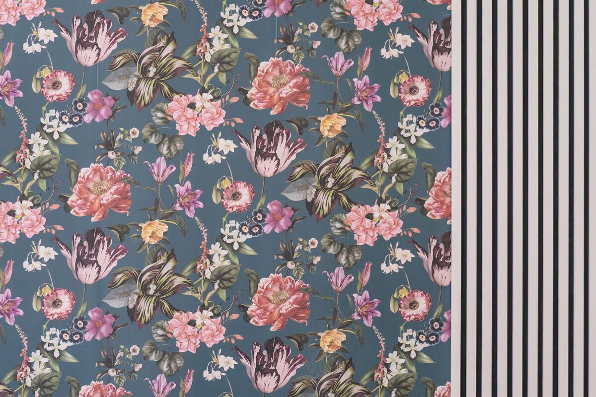 Een slaapkamer met bloemenbehang, een blauw bed met passende kussens en een nachtkastje met een lamp.