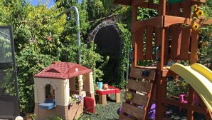 Uma área de recreação infantil com uma casinha, estrutura de escalada e um escorrega.