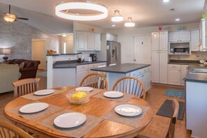 A modern kitchen with white cabinets, a central island, and a dining area with a wooden table and chairs.