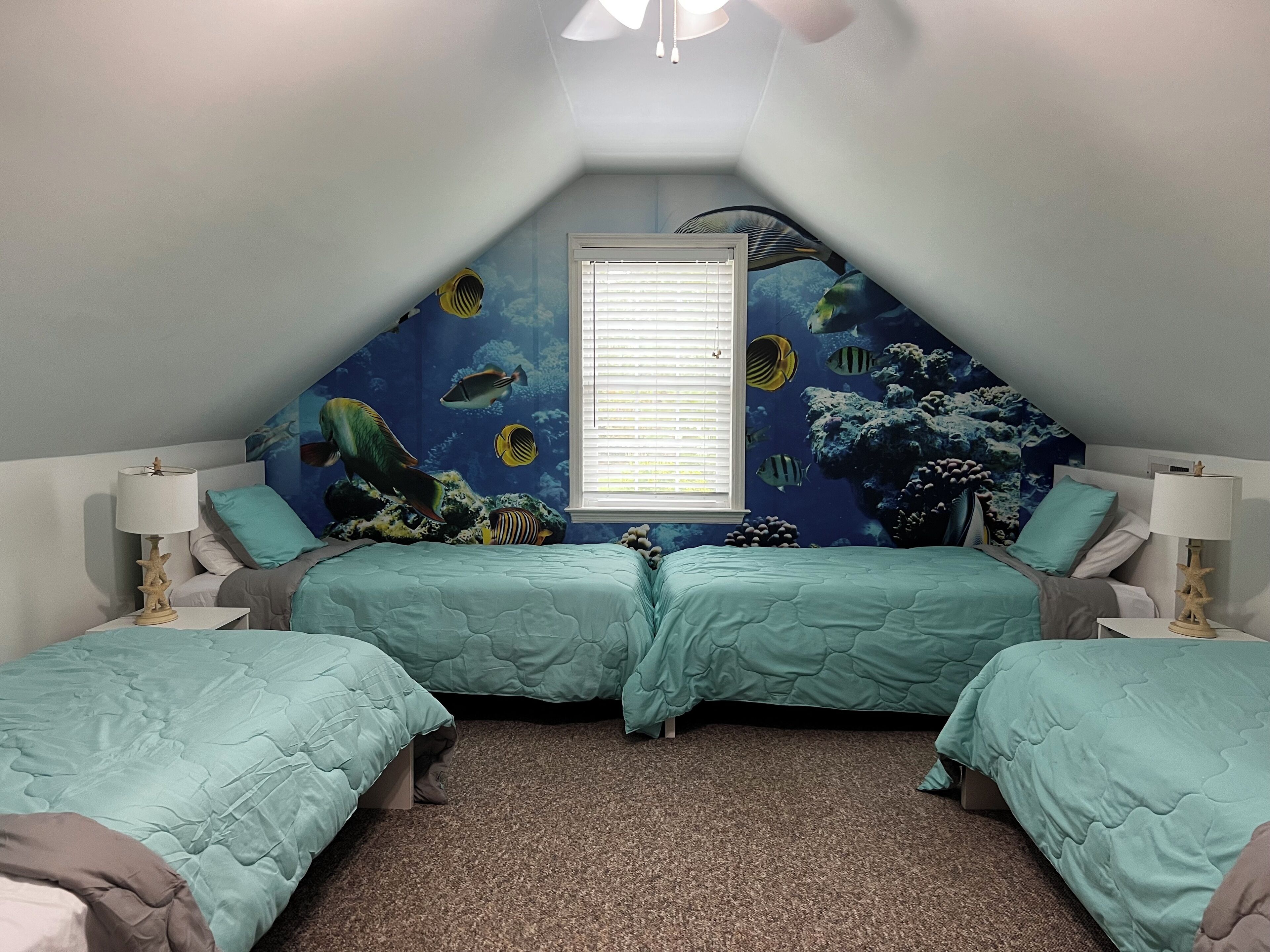 Een slaapkamer met twee bedden, een raam met zonwering en een muurschildering met zeethema.