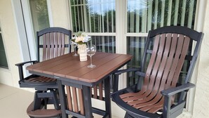 Una mesa de patio con cuatro sillas, un florero con flores y dos copas de vino.
