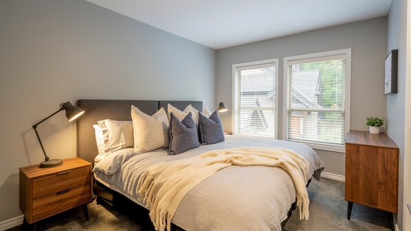 A bedroom with a bed, bedside tables, a nightstand, a window with blinds, and a small plant on a dresser. - True Ski-In/Out | Modern 3BR | Mountain Views | Communal Hot Tub | Managed by Aloha Whistler (Whistler)