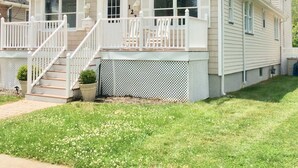 Ein zweistöckiges Haus mit Veranda, Treppe und kleinem Garten.