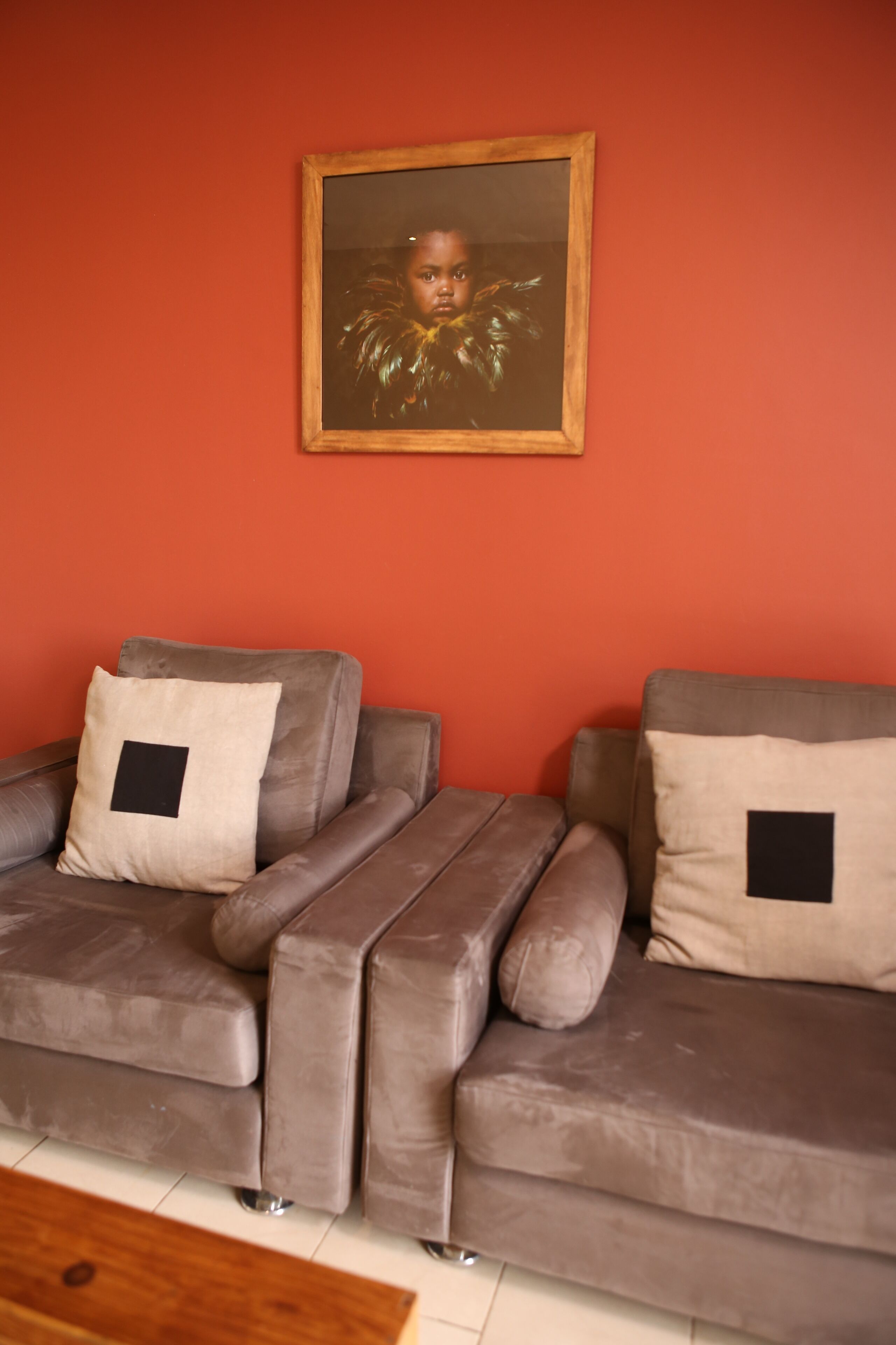 A living room with a brown sofa set against a red wall, a framed picture above the sofa, and a wooden coffee table in the foreground.