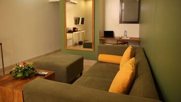 Una habitación de hotel moderna con un sofá verde, una mesa de centro de madera y un espejo que refleja una zona de cocina.