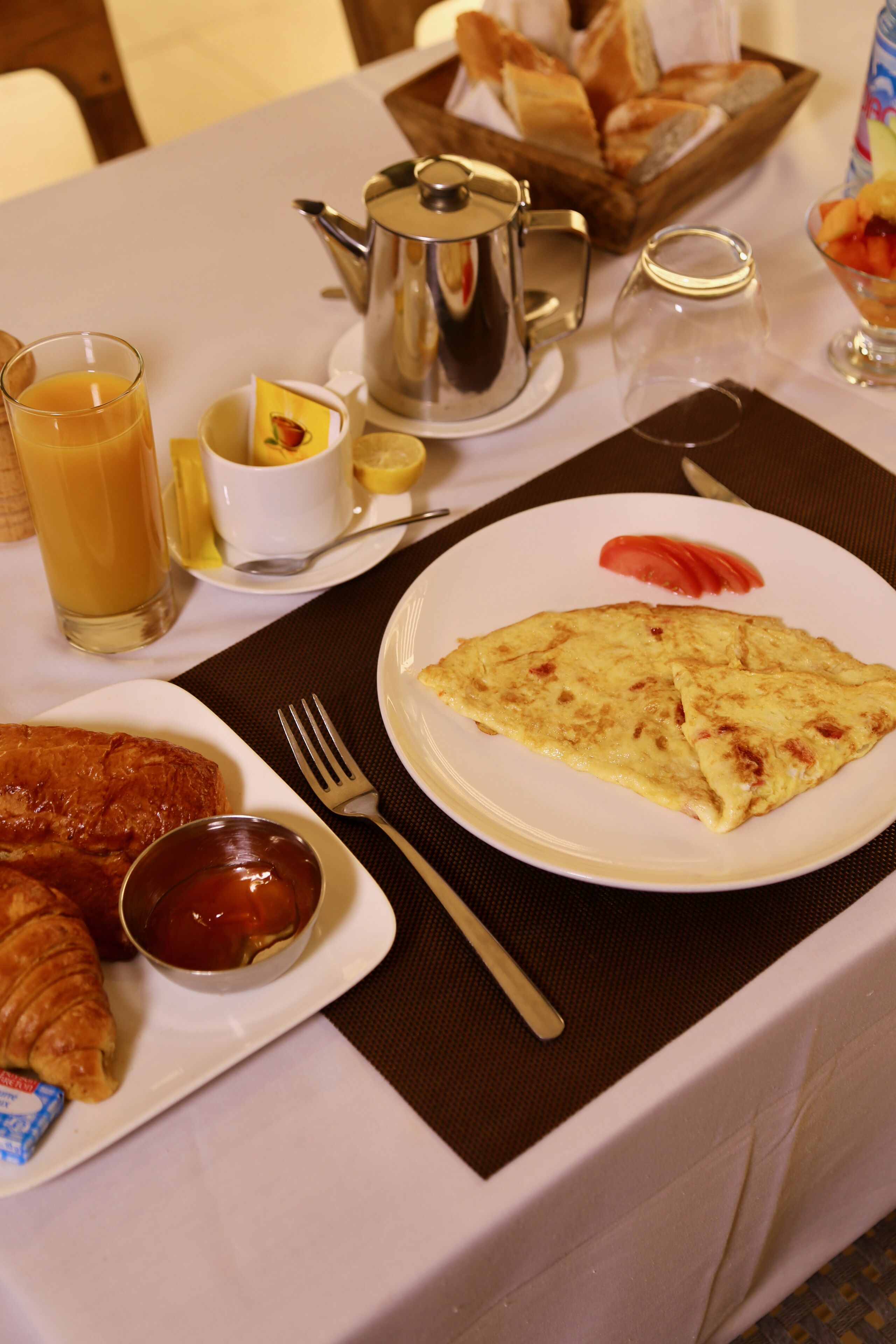 Una mesa de desayuno con un plato de huevos, croissants y un vaso de zumo de naranja.