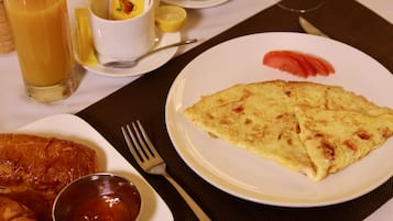 Una mesa de desayuno con un plato de huevos, croissants y un vaso de zumo de naranja.