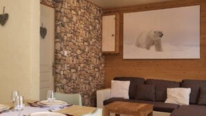 Una zona de estar acogedora con pared de piedra, un sofá de madera, una mesa de comedor con sillas y un cuadro de un oso polar en la pared.