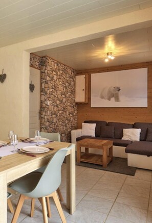 Una zona de estar acogedora con pared de piedra, un sofá de madera, una mesa de comedor con sillas y un cuadro de un oso polar en la pared.