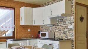 Una cocina acogedora con armarios de madera, una pared de acento de piedra y una zona de comedor con una mesa preparada para cuatro personas.