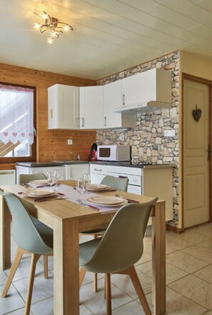 Una cocina acogedora con armarios de madera, una pared de acento de piedra y una zona de comedor con una mesa preparada para cuatro personas.