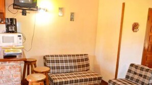 A cozy room with a television, a microwave, and a small table with a chair. There are two plaid sofas and a wooden stool.