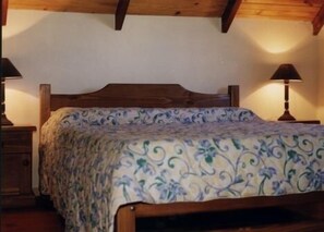 Un dormitorio con cabecera de madera, colcha estampada y dos lámparas de noche.