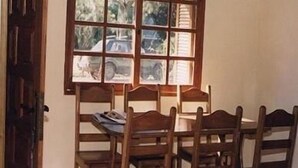 A dining area with a wooden table and chairs, a window with multiple panes, and a door to the left.