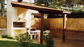 A patio area with a grill, white chairs, and a wooden fence.