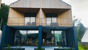 A modern two-story house with a sloped roof, large windows, and a balcony with white railings. - FURNAS HOUSES South (19A) (FURNAS)