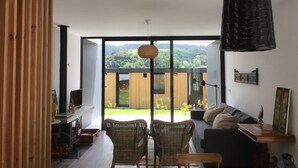 A modern living room with a large sliding glass door leading to a balcony with a view of green hills. - FURNAS HOUSES South (19A) (FURNAS)