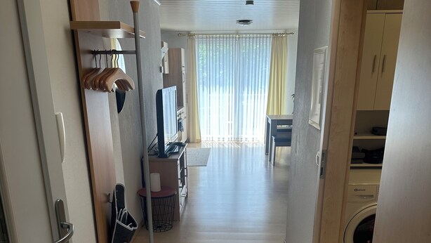 A hallway with a tiled floor, a wooden door, a coat rack, a television, and a washing machine. - Susi's Apartment - 60m2 for 2 persons, quiet location and handicapped accessible (Waldgirmes)