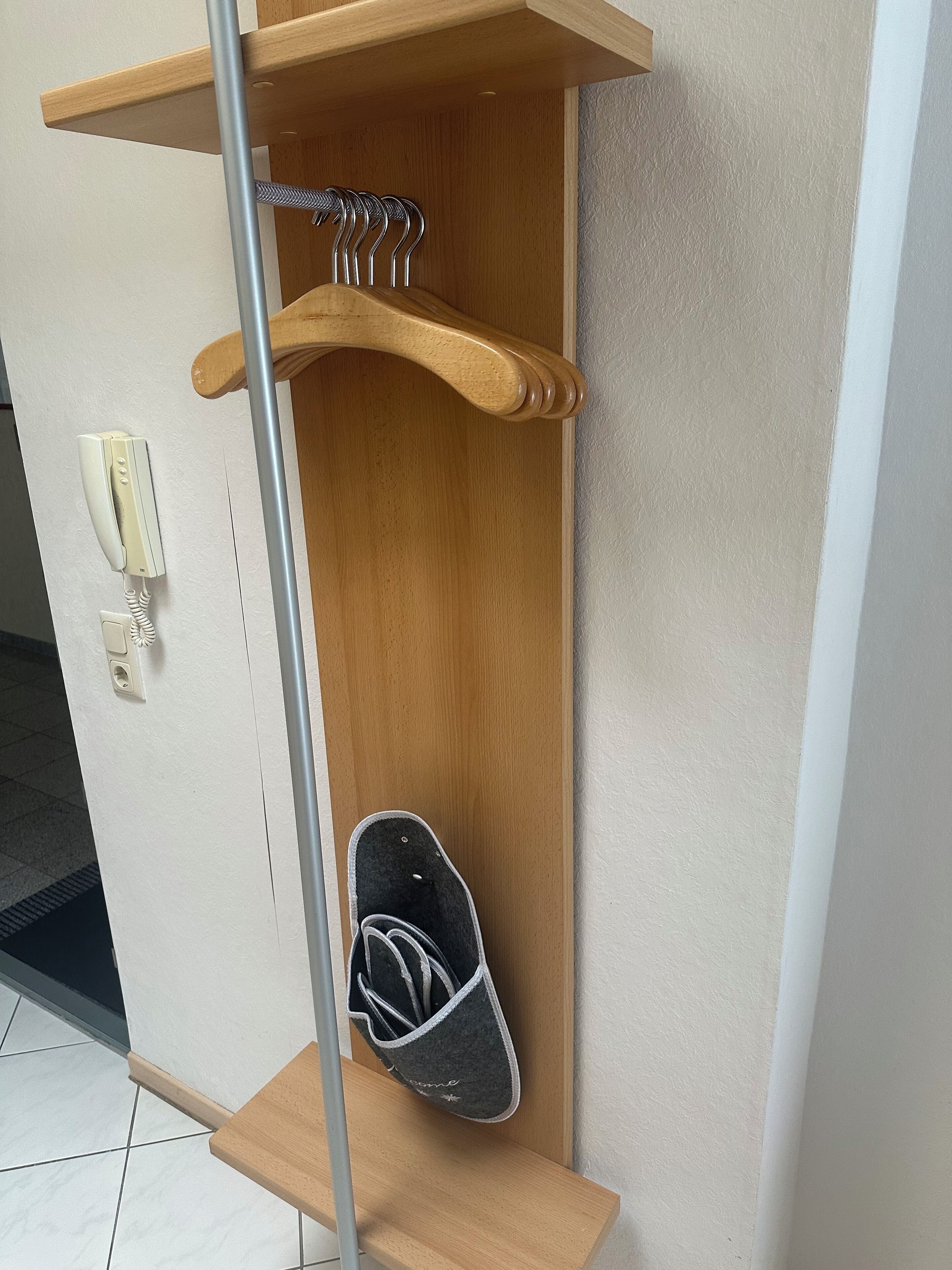 Un porte-chaussures en bois, avec une paire de chaussons et un téléphone.