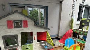 A children's playhouse with a slide, a small kitchen set, and a hanging swing. - Susi's Apartment - 60m2 for 2 persons, quiet location and handicapped accessible (Waldgirmes)