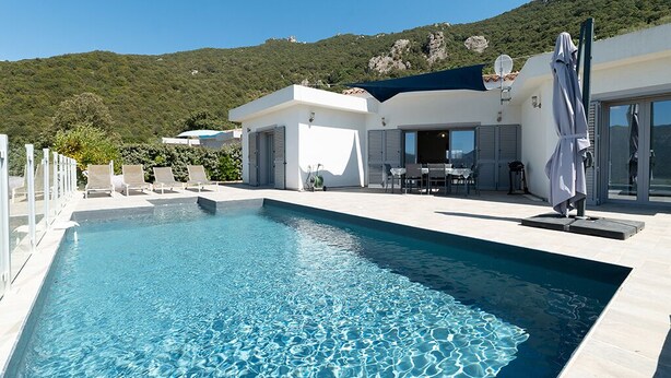 A swimming pool with a mountain backdrop, outdoor seating, and a covered patio area.