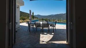 An open door to an outdoor patio with a pool, dining table, and chairs.