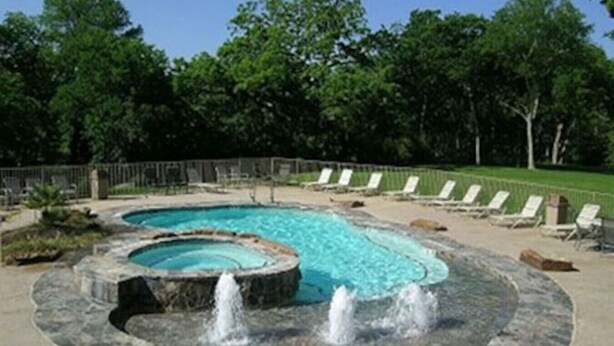 A swimming pool with a hot tub and a fountain, surrounded by lounge chairs and a fence. - Good Night Sleep Tight | Guadalupe Riverfront | WiFi | Pools (New Braunfels)