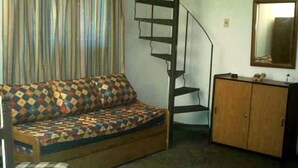 Une pièce comprenant un canapé-lit, une armoire en bois, un escalier en colimaçon et un miroir au mur.
