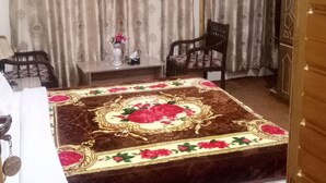 A room with a bed, a chair, a small table with a vase, and curtains. - Hunza holiday Inn (Karimabad)