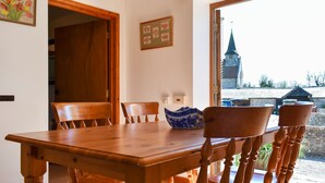 A wooden dining table with six chairs, a wooden ceiling with exposed beams, and a view of a church through a window. - 2 bedroom accommodation in Compton, near Chichester (Compton, near Chichester)