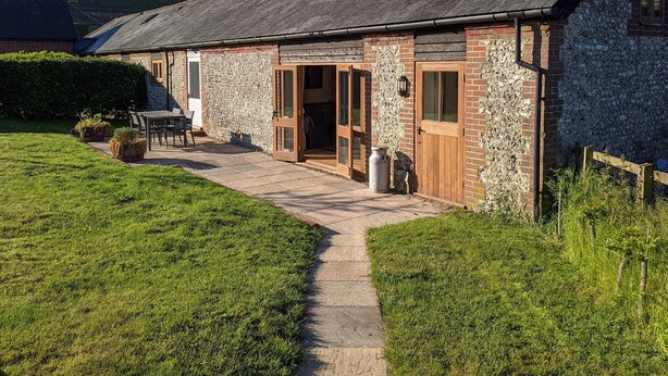 A stone house with a wooden door and a small patio with a table and chairs. - 2 bedroom accommodation in Compton, near Chichester (Compton, near Chichester)