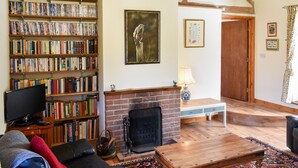 A cozy living room with a fireplace, a bookshelf filled with books, a television, and a comfortable seating area. - 2 bedroom accommodation in Compton, near Chichester (Compton, near Chichester)