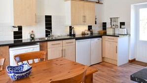 A modern kitchen with wooden cabinets, a black countertop, and a wooden dining table. - 2 bedroom accommodation in Compton, near Chichester (Compton, near Chichester)