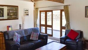 A cozy living room with a leather sofa, a wooden coffee table, and a bookshelf filled with books. - 2 bedroom accommodation in Compton, near Chichester (Compton, near Chichester)