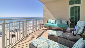 Un balcon avec vue sur la plage, des meubles en osier et une bouteille de vin.