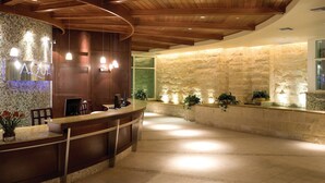 Un espace d’accueil comprenant un comptoir de réception en bois, un mur décoré de mosaïques et un mur en pierre agrémenté de plantes.